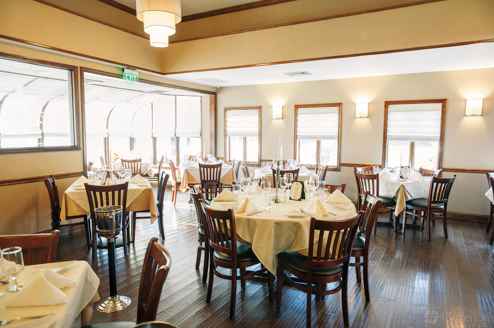 A restaurant dining room with wood floors, round tables set with white linens, and natural light at Il Luogo Ristorante.