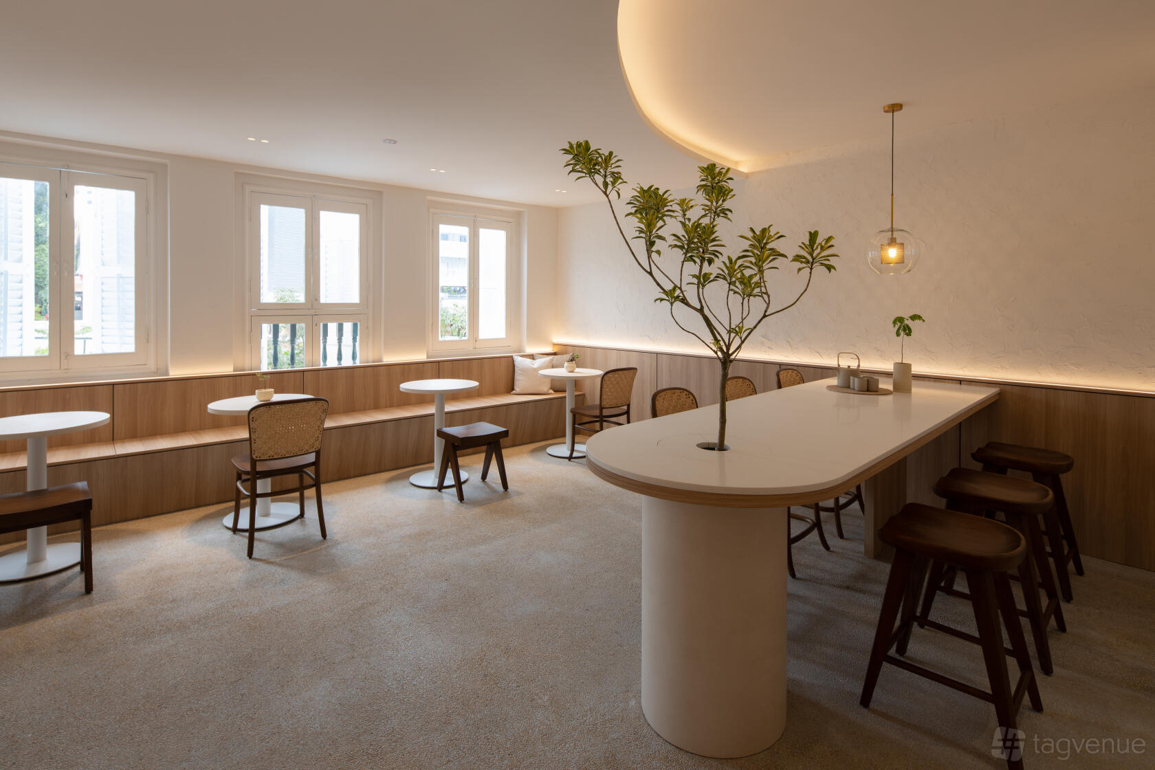 A restaurant with white round tables, wooden chairs, a central island table, and large windows at Arc-en-ciel Pâtisserie.