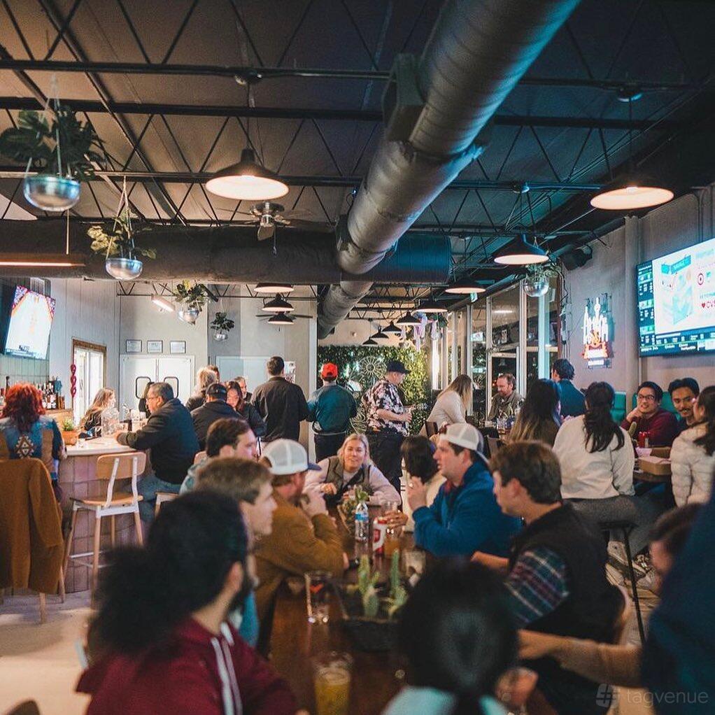 An event space in a bar with hanging plants, exposed ductwork, and communal tables at LadyBird Beer Garden.