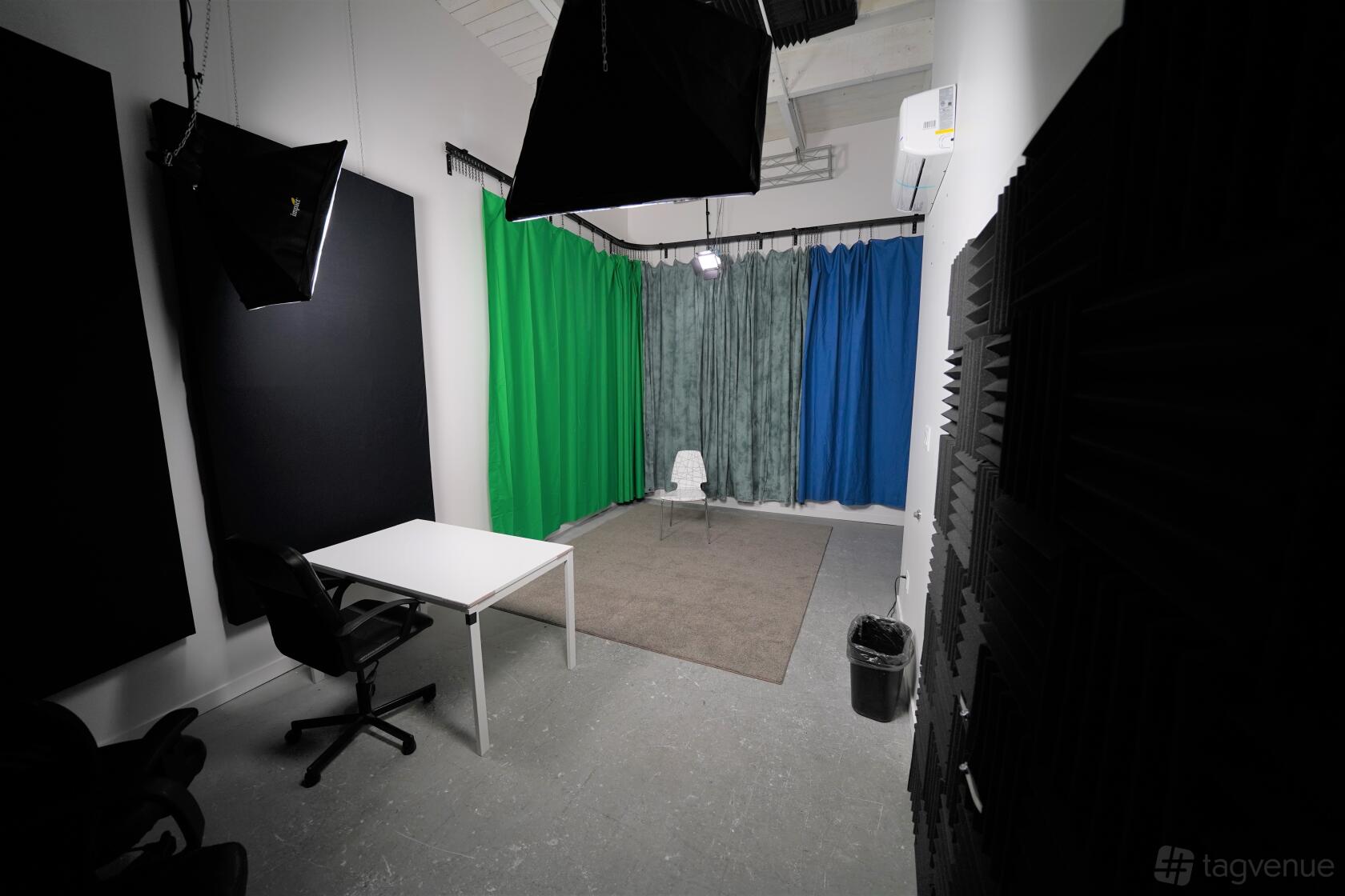 A film studio with green and blue curtains, a white desk, and overhead softbox lights at Shoreline Studios.