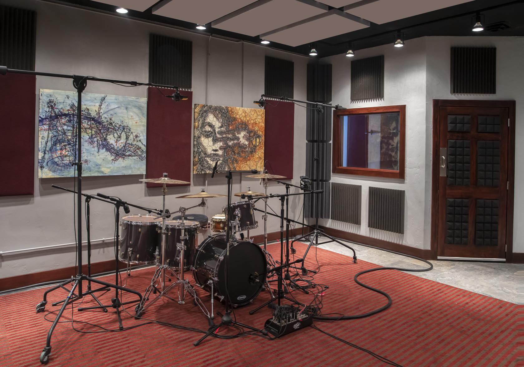 A recording studio with a drum kit, microphones, acoustic panels, and wall art at Electric Shop Recording.
