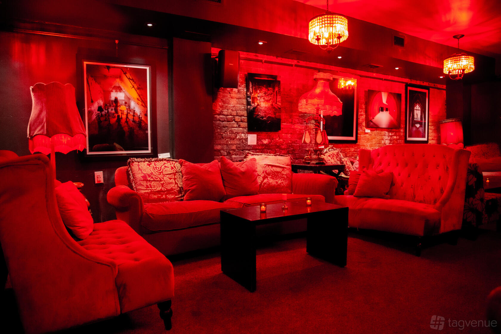 A lounge with red velvet sofas, exposed brick walls, and ambient red lighting at Madame X.