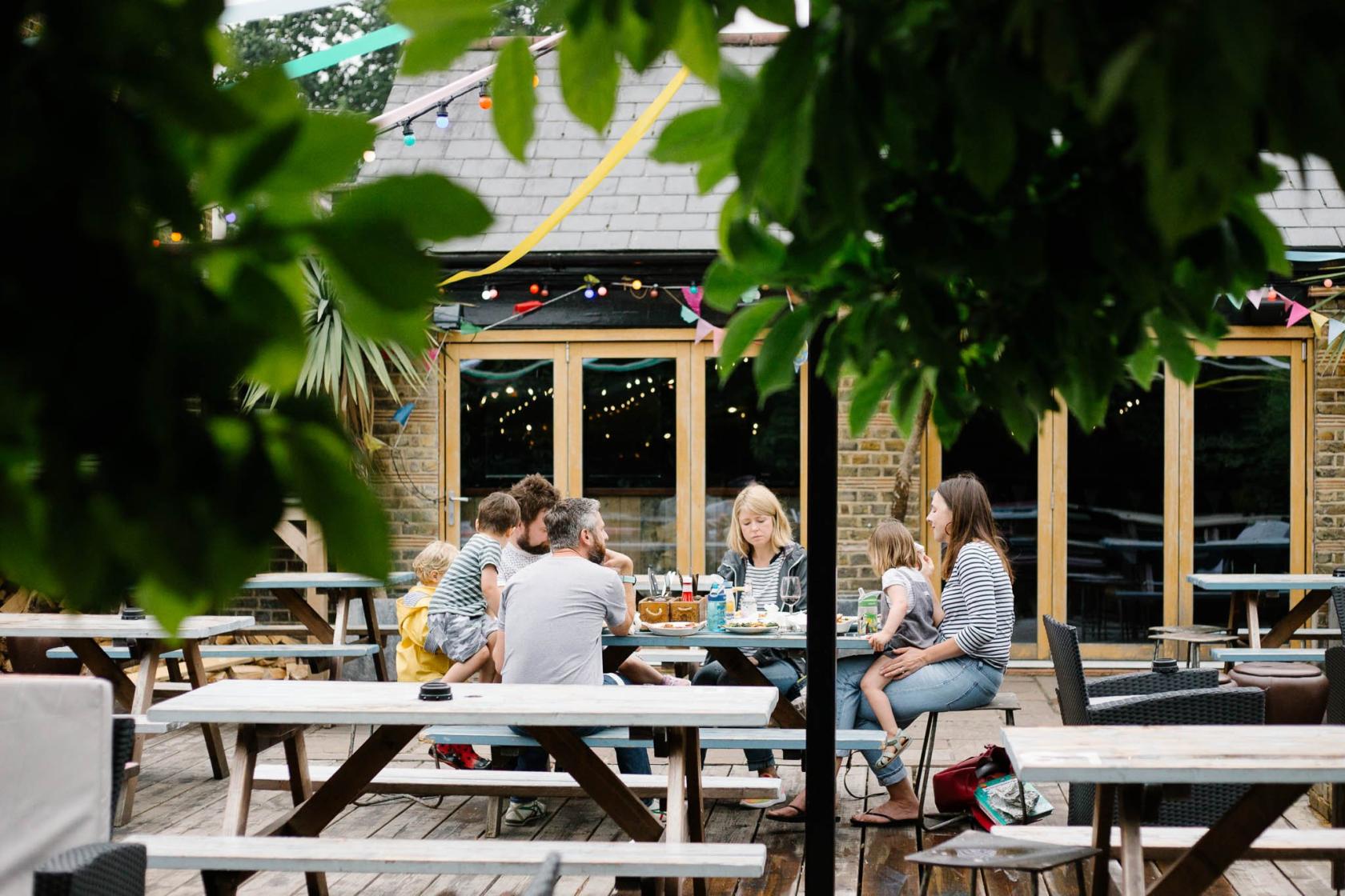 An outdoor pub space with wooden picnic tables, string lights, and colorful bunting at Watson's Telegraph