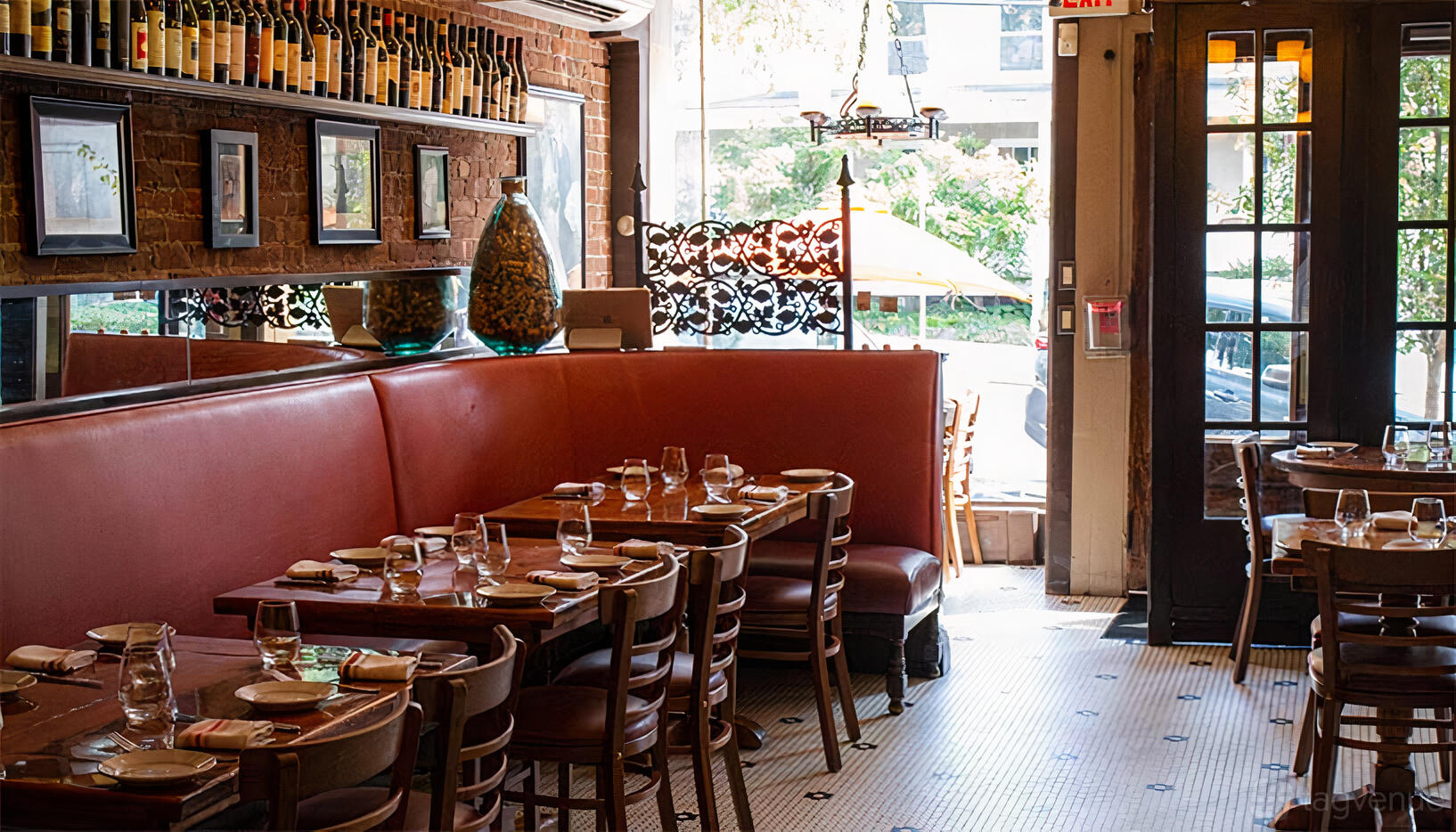 A restaurant with red leather banquette seating, white tiled floors, and wine bottles displayed on shelves at Mima Vinoteca.