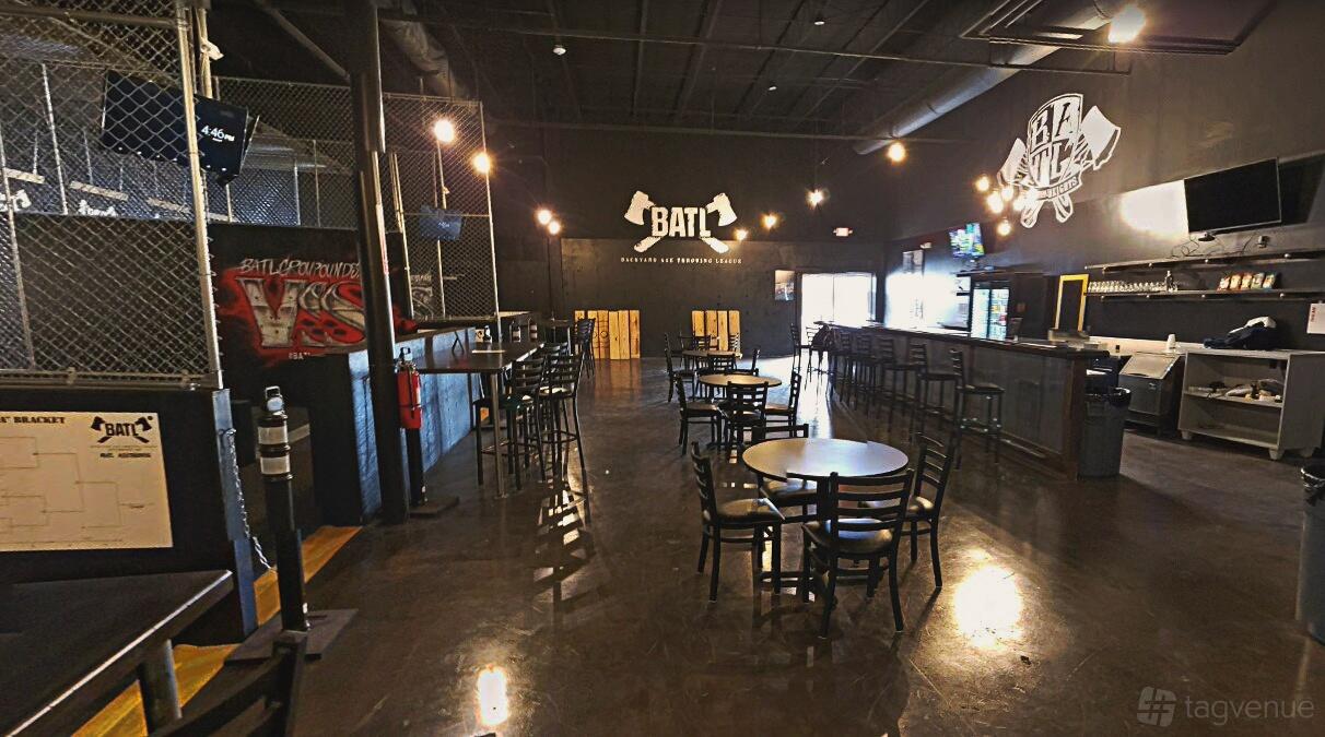 A sports club with black tables and chairs, a bar, and axe-throwing lanes at BATL Grounds Houston.
