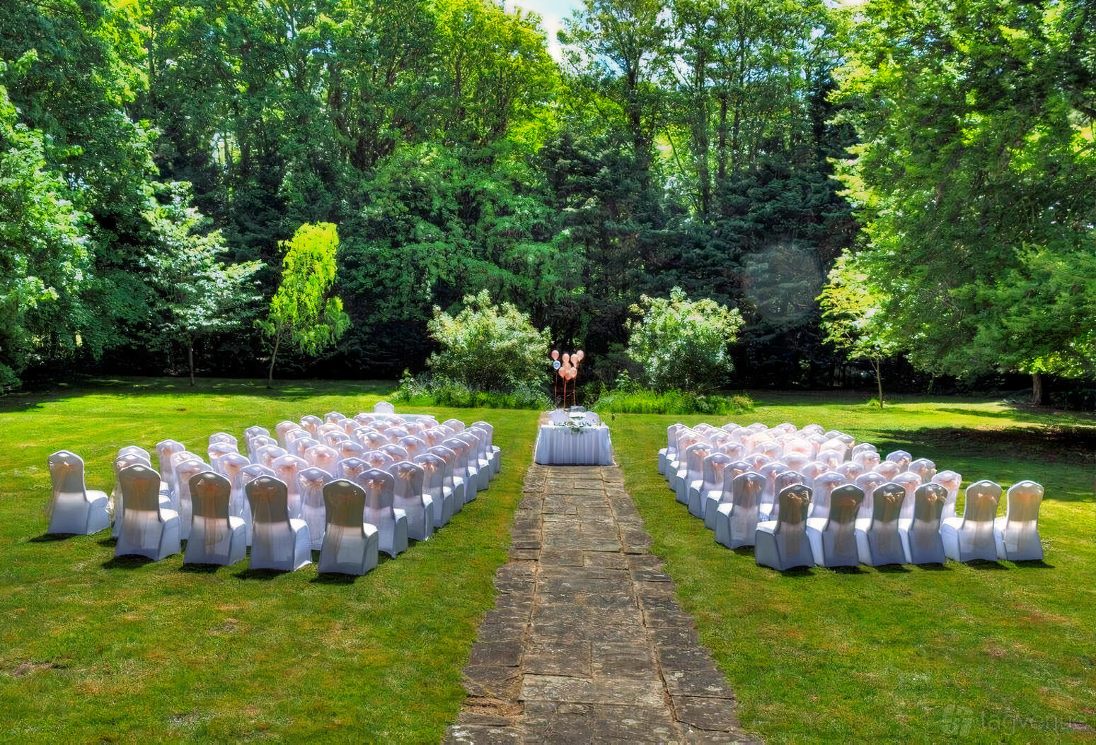 A garden event space with rows of white-covered chairs and a stone aisle at The Grange Country House Hotel.