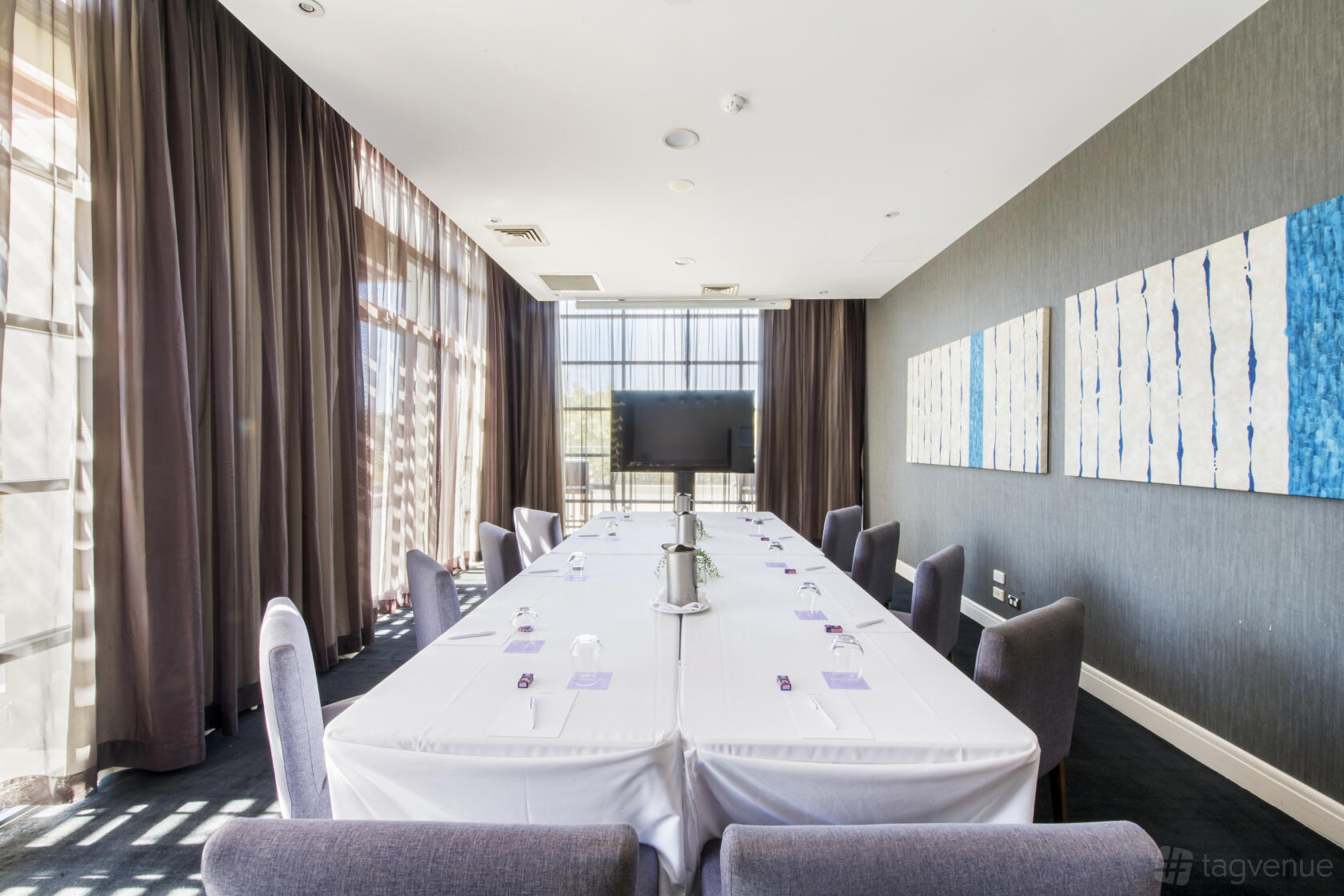 A boardroom with a long table, grey chairs, floor-to-ceiling windows, and wall art at Mercure Kooindah Waters.