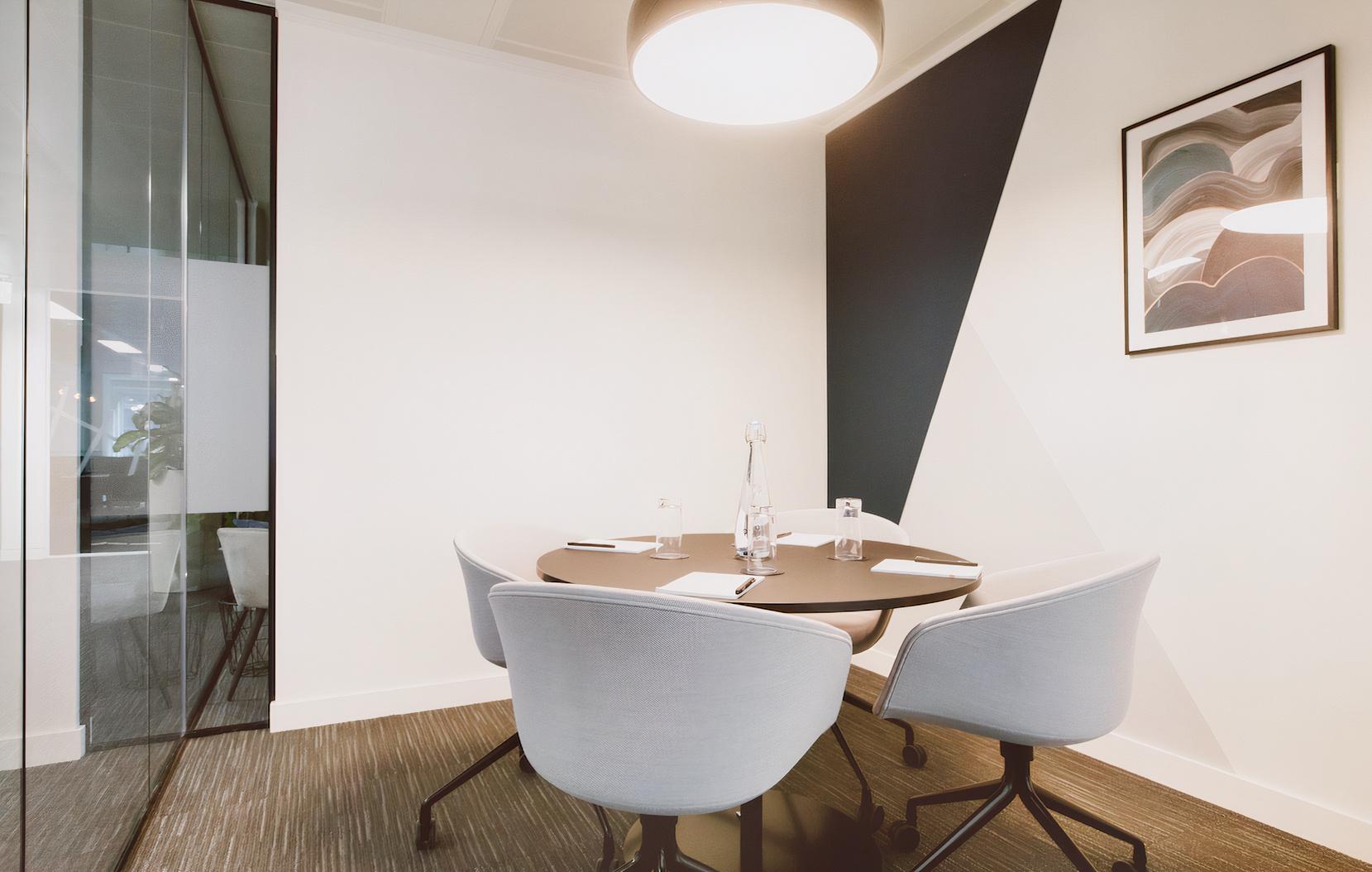 A meeting room with a round table, four modern chairs, geometric accent wall, and pendant light at Orega Old Bailey.
