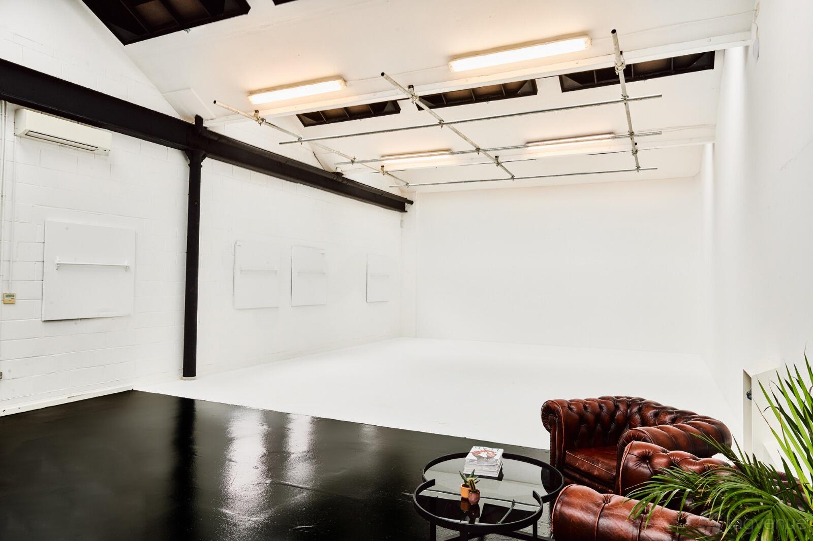 A photo studio with white cyclorama walls, high ceilings, skylights, and a leather sofa seating area at GAS Studios.