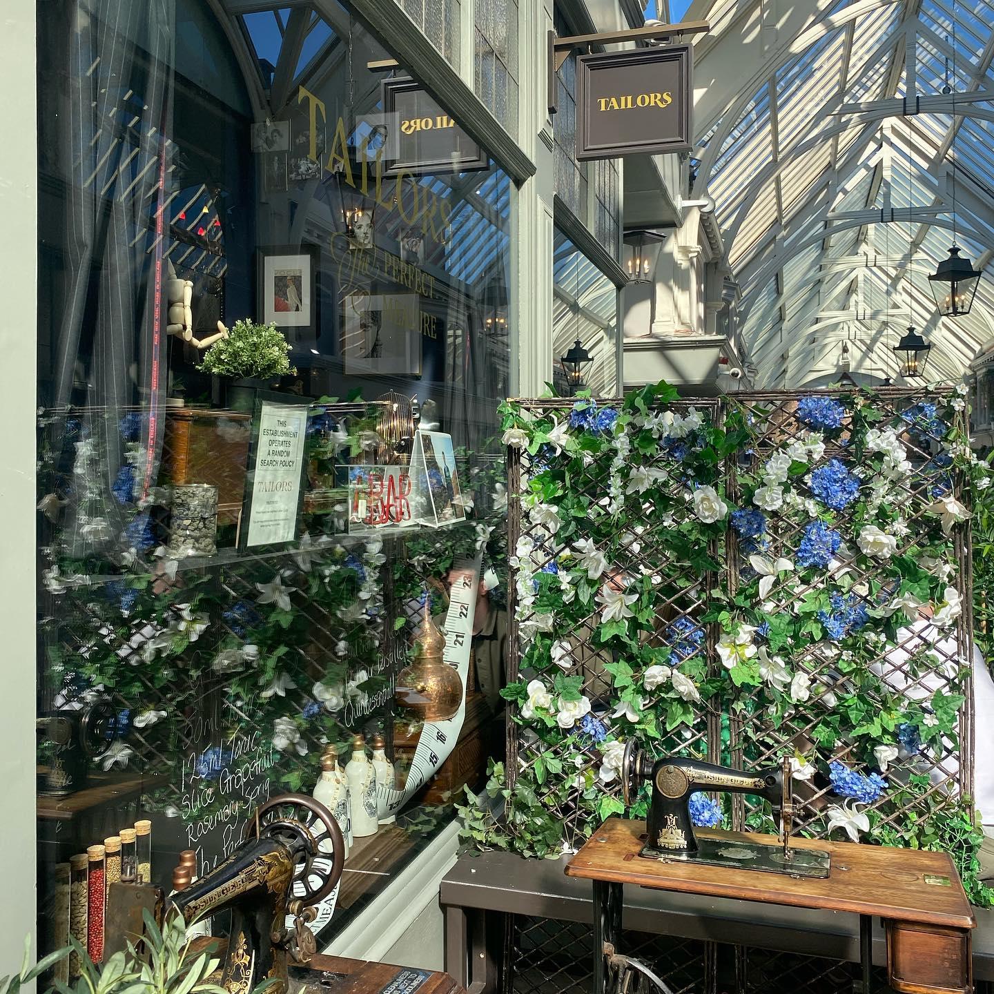 A pub with floral trellis decor and vintage distilling equipment displayed by large windows at Tailors Gin.