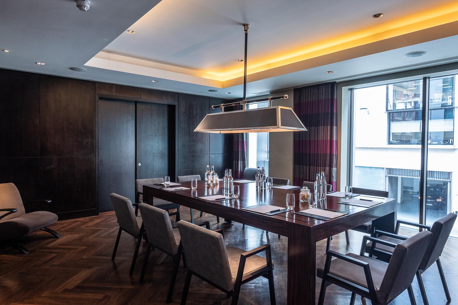 A hotel dining room with a rectangular wooden table, upholstered chairs, and floor-to-ceiling windows at South Place Hotel.