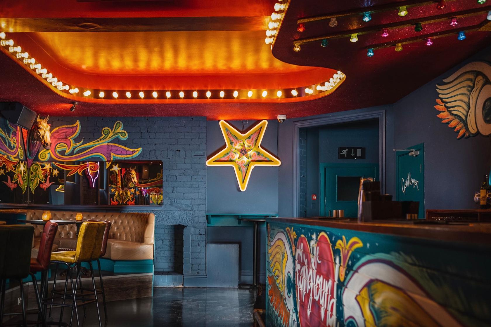 An event space in a bar with colorful graffiti walls, plush seating, and a neon star sign at Cuckoo.
