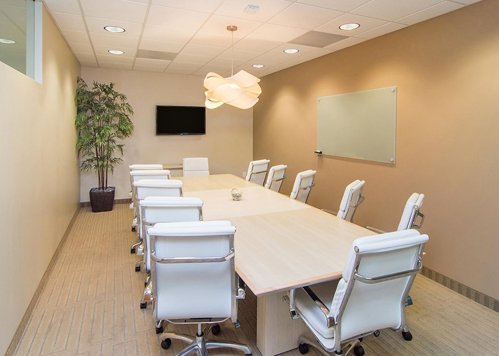 A meeting room with a long light wood table, white leather chairs, wall-mounted TV, and whiteboard at Premier Workspaces - The Atrium.
