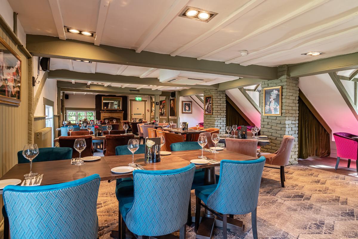 A dining room with colorful upholstered chairs, set tables, and exposed beams at The Queen & Castle.