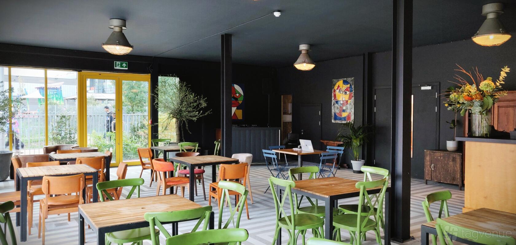 An event space in a restaurant with colorful mismatched chairs, wooden tables, and large windows at Hackney Bridge.