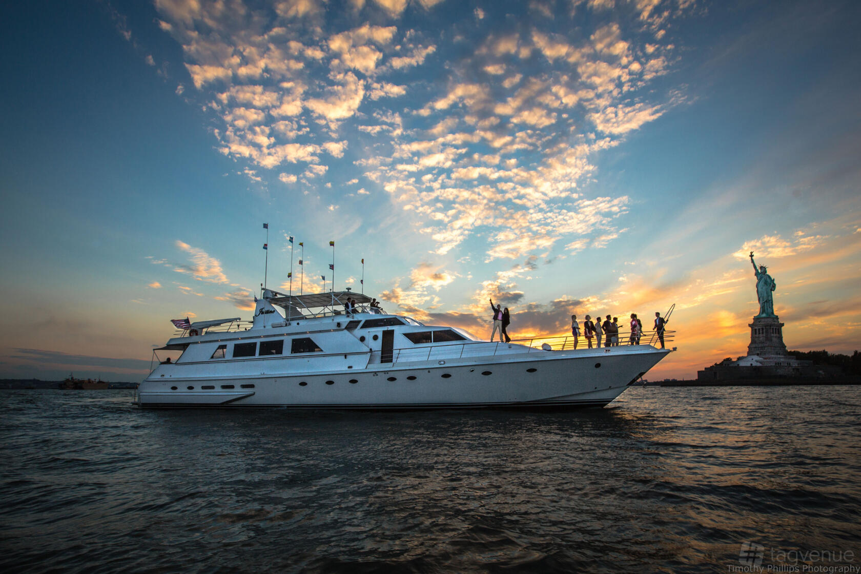 A yacht with an open deck and guests enjoying sunset views near the Statue of Liberty at Del Rio Yacht Charter.