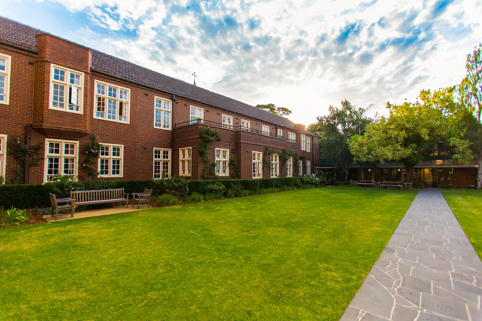 An academic venue with red brick exterior, white-trim windows, and benches facing a large lawn at University College.