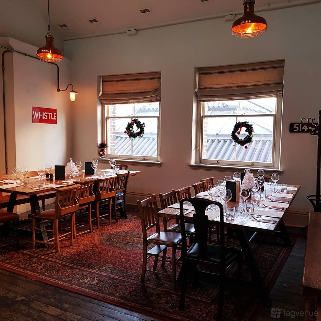 A pub dining area with wooden tables, set for a meal, large windows, and festive wreaths at The Parcel Yard.