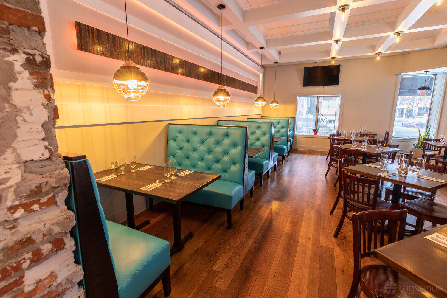 A dining room with turquoise tufted booths, wood flooring, and pendant lighting at Cantina 'Calaca' Feliz.