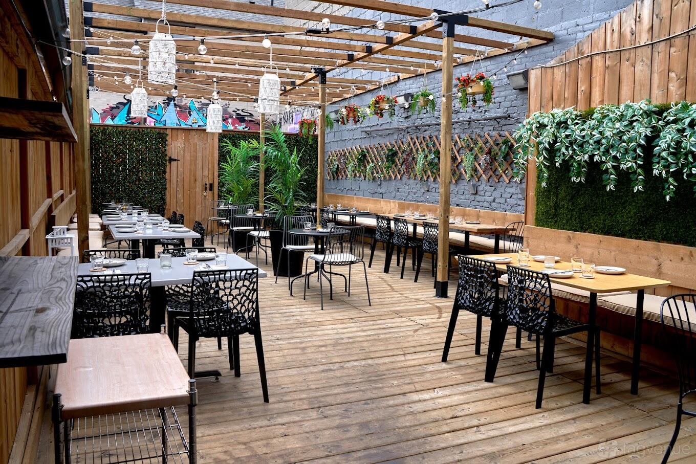 An outdoor dining area with wooden decking, pergola, hanging lights, and greenery at Nuna Kitchen + Bar.