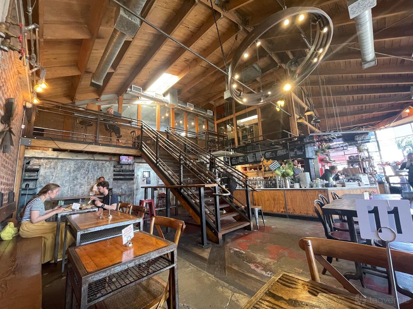 A cafe with exposed wood ceilings, metal staircase, chalkboard menus, and mixed seating at Paper or Plastik Cafe.