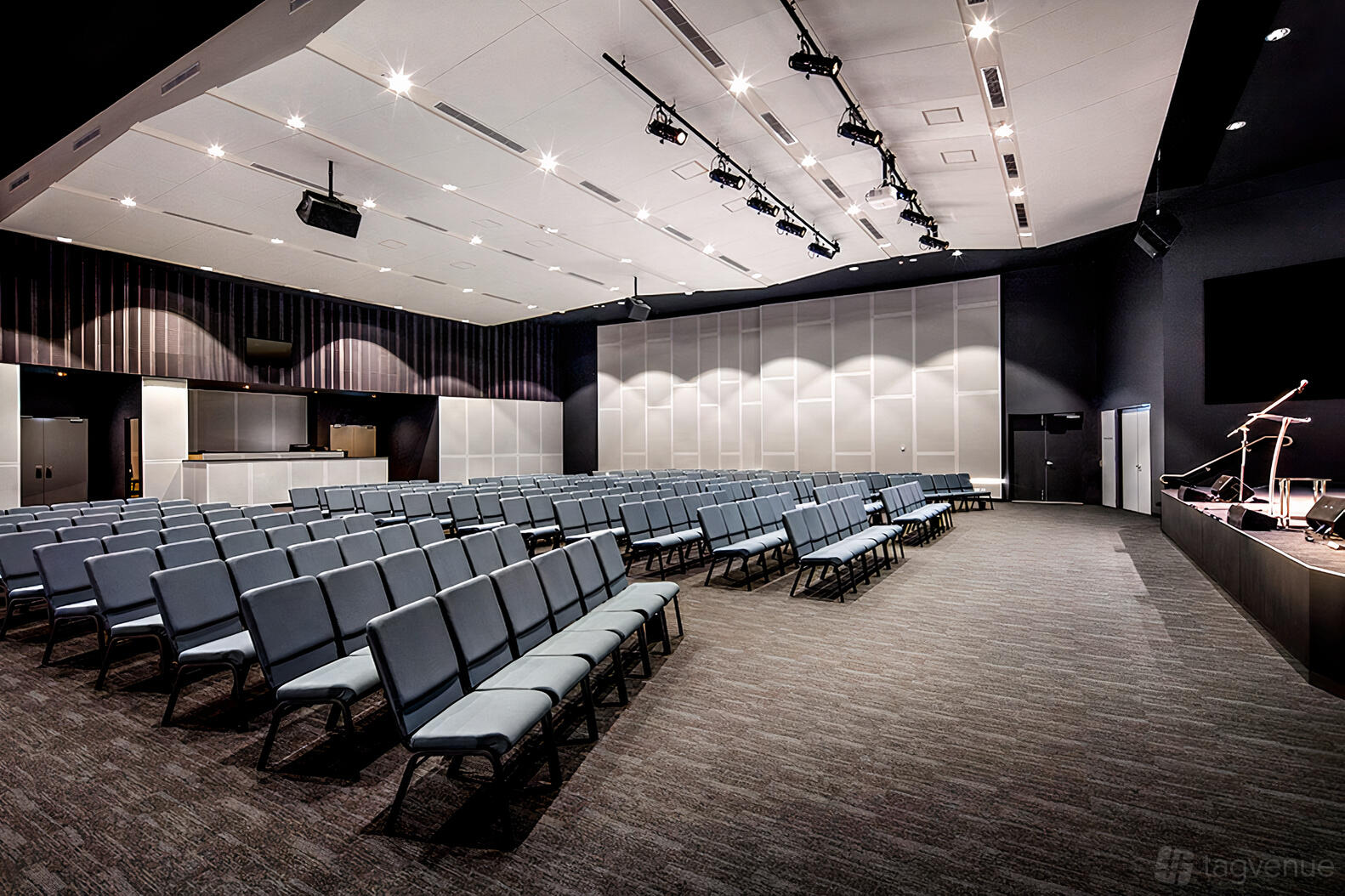 An auditorium with tiered rows of cushioned chairs, stage area, and overhead lighting at Uni Hill Conference Centre.