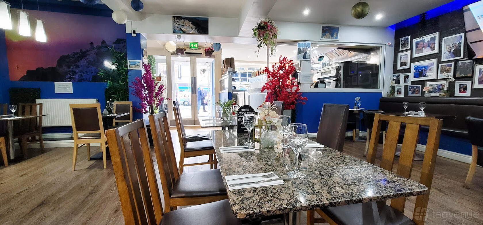 An event space in a restaurant with granite-topped tables, wooden chairs, floral centerpieces, and blue accent walls at Athens Greek Restaurant.