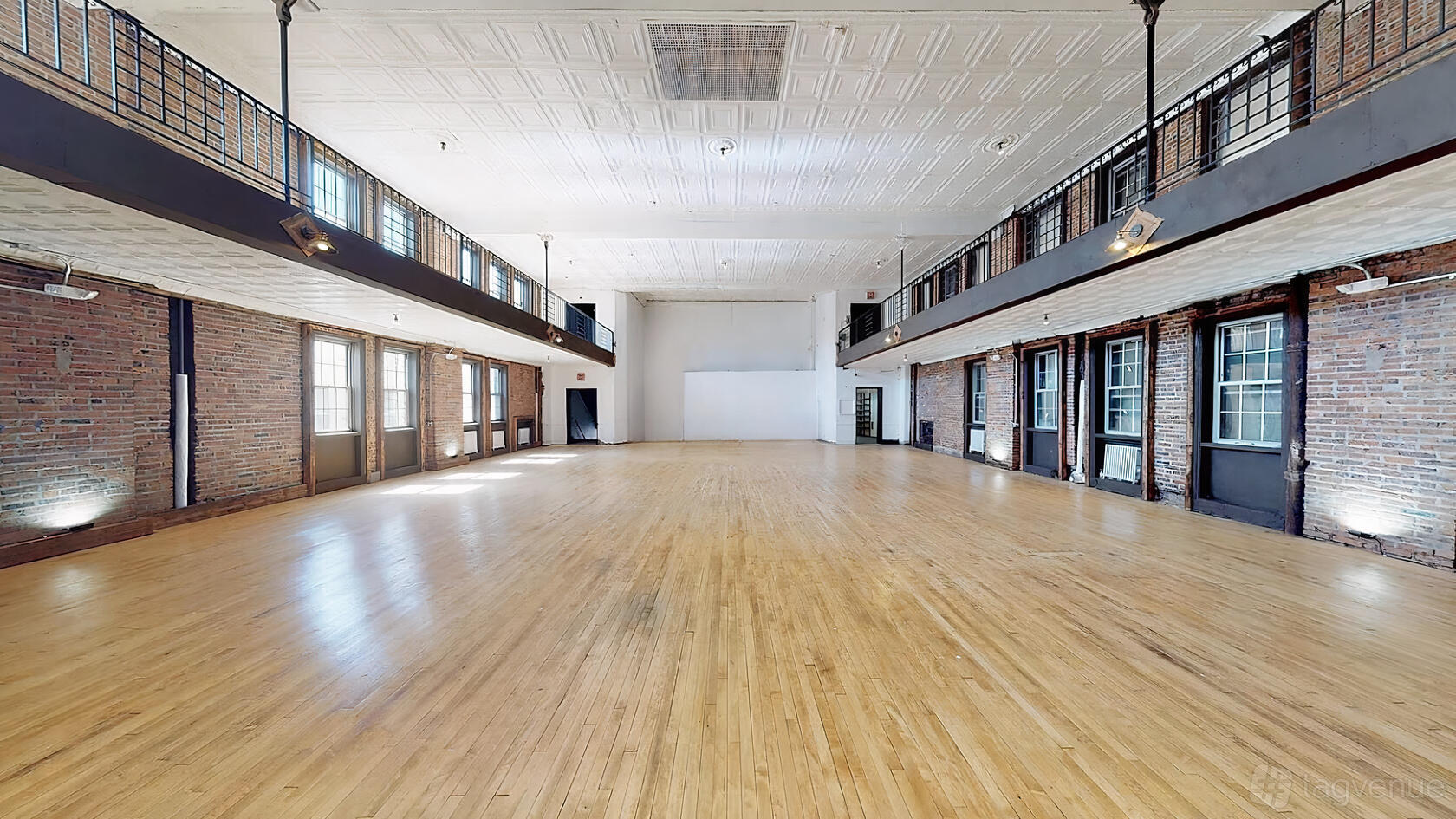 An event venue with exposed brick walls, tall windows, and a spacious hardwood floor at Tammany House.