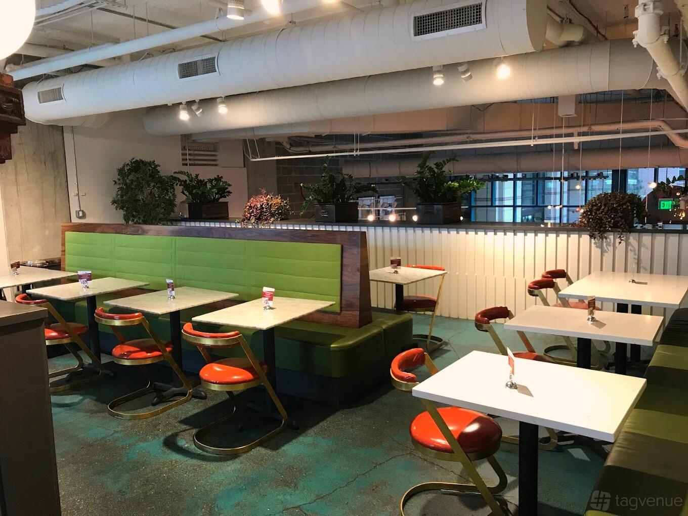 An event space in a restaurant with green banquettes, red chairs, potted plants, and overhead lighting at Local Foods - Tanglewood.