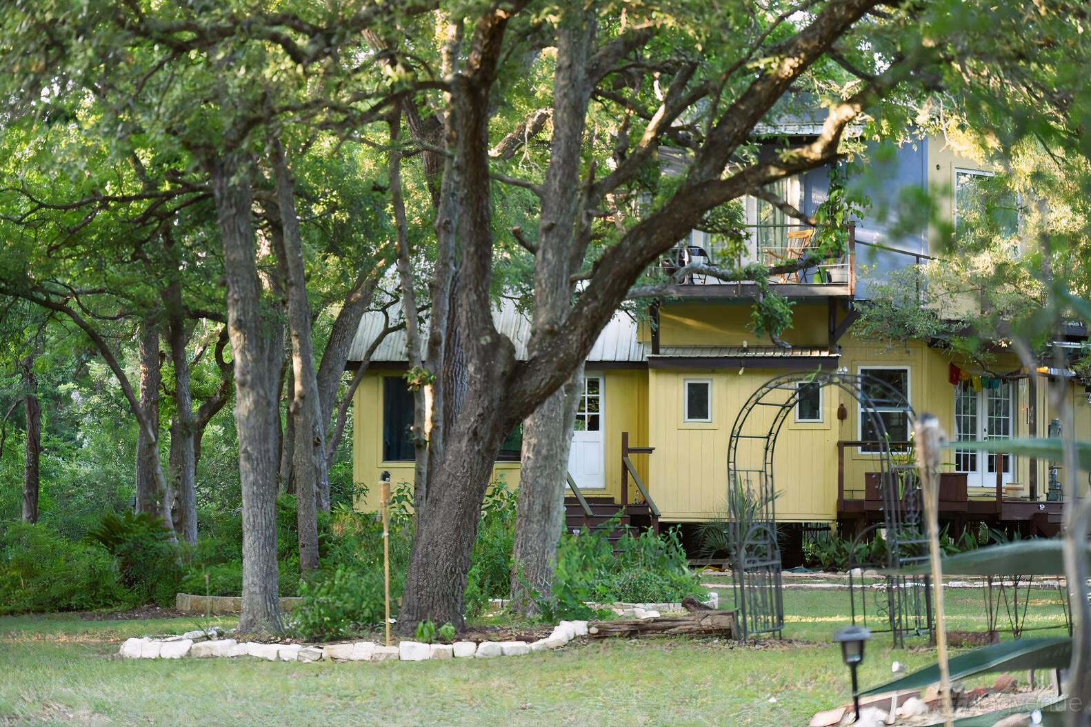 A versatile event space with a yellow house, mature trees, and a garden archway at Lotus Bend Sanctuary.