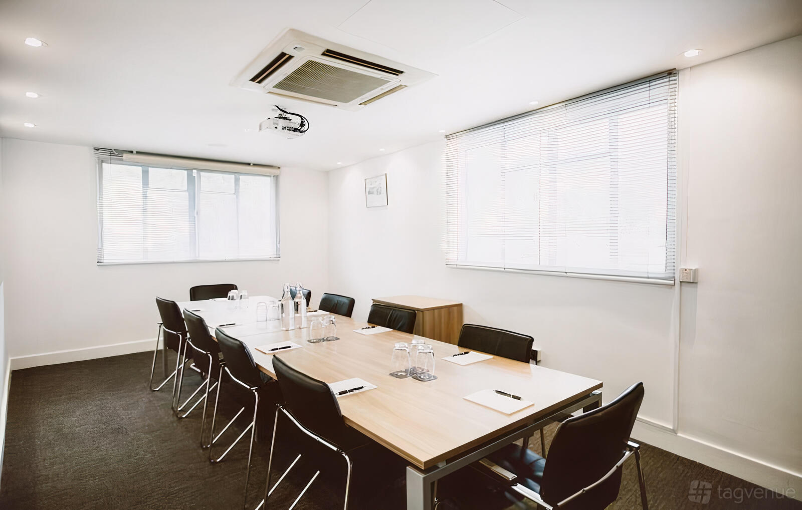 A meeting room with a long wooden table, black chairs, and large windows with blinds at Orega - The Beehive - Gatwick.