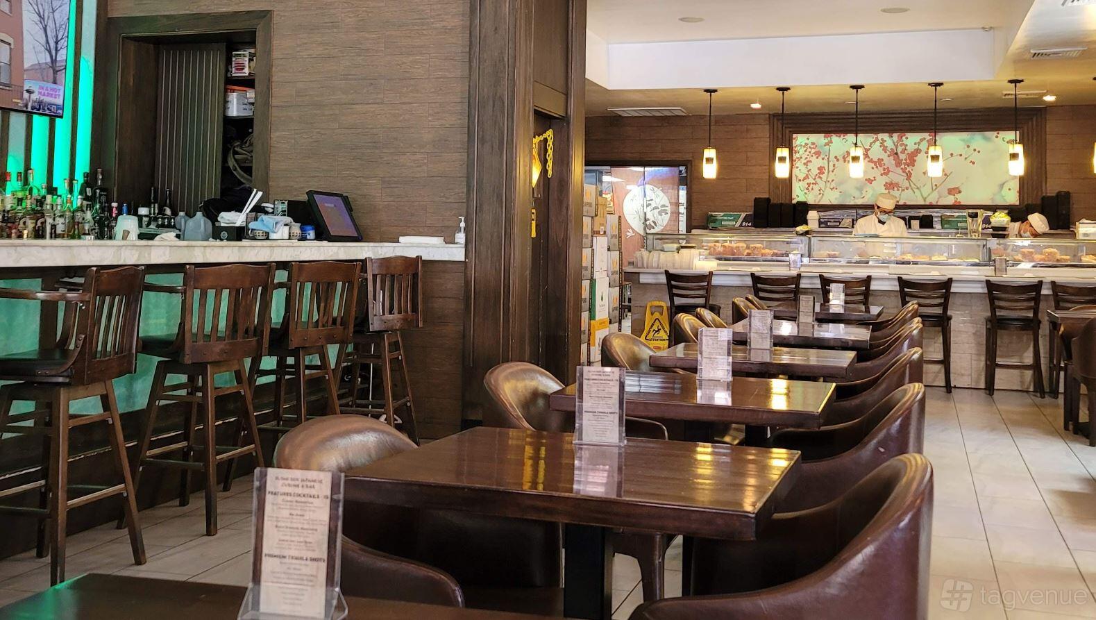 A restaurant dining area with dark wooden tables, leather chairs, and a sushi bar counter at Sushi Ren.