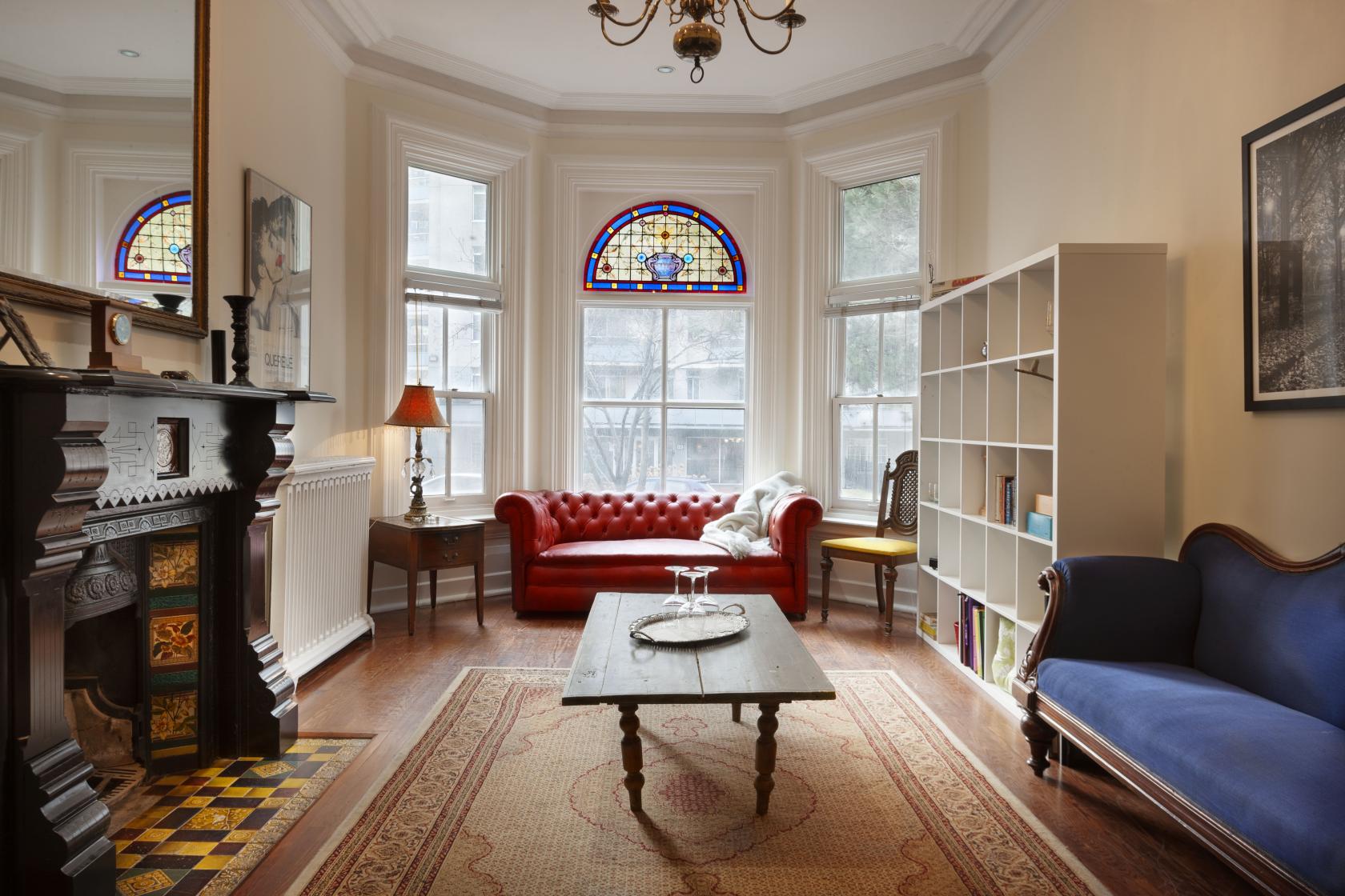 A meeting room with bay windows, stained glass, a red tufted sofa, and a decorative fireplace at Foy House.