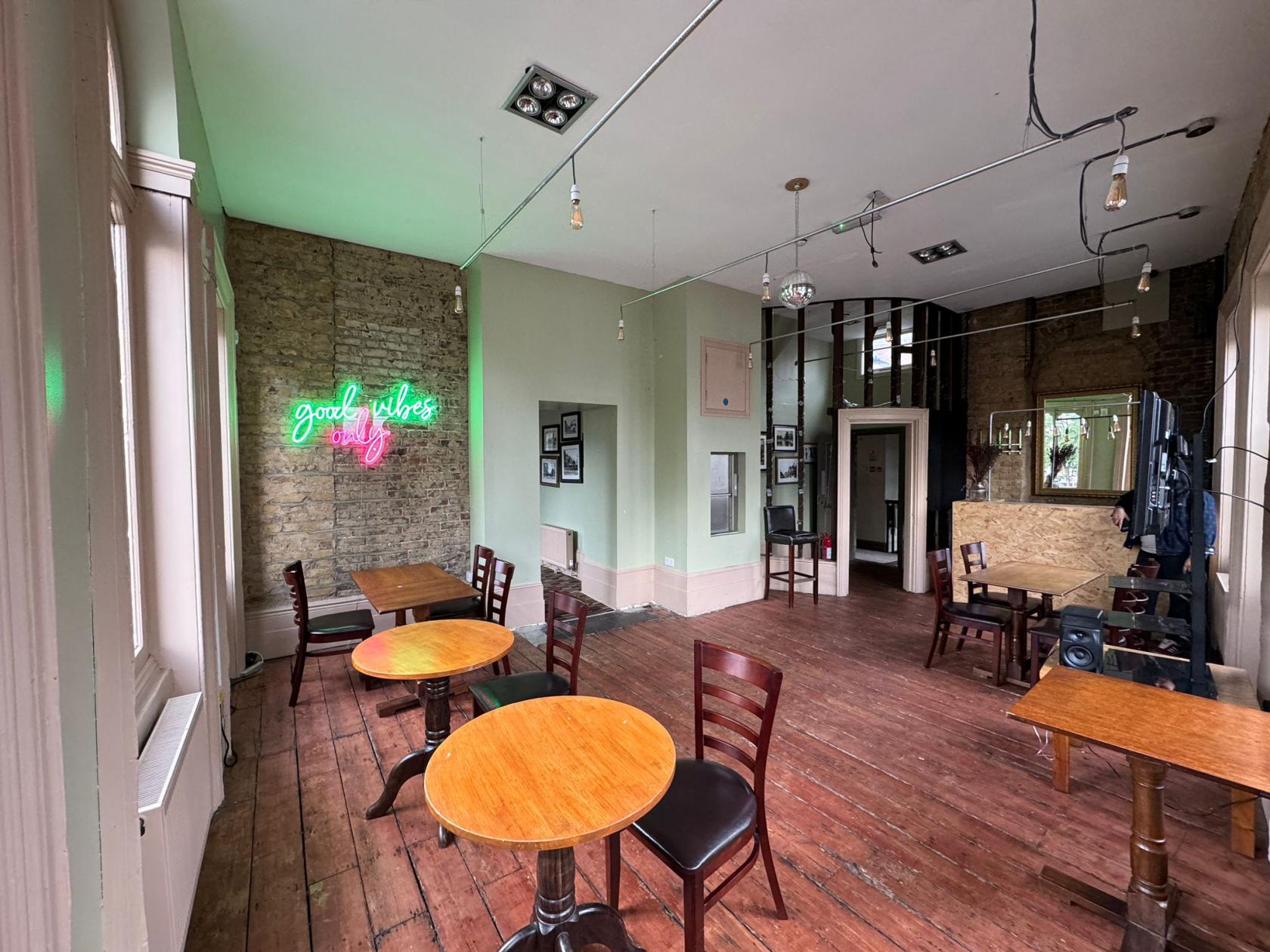 A function room in a pub with exposed brick walls, wooden floors, round tables, and a neon sign at THE PHOENIX PUB.