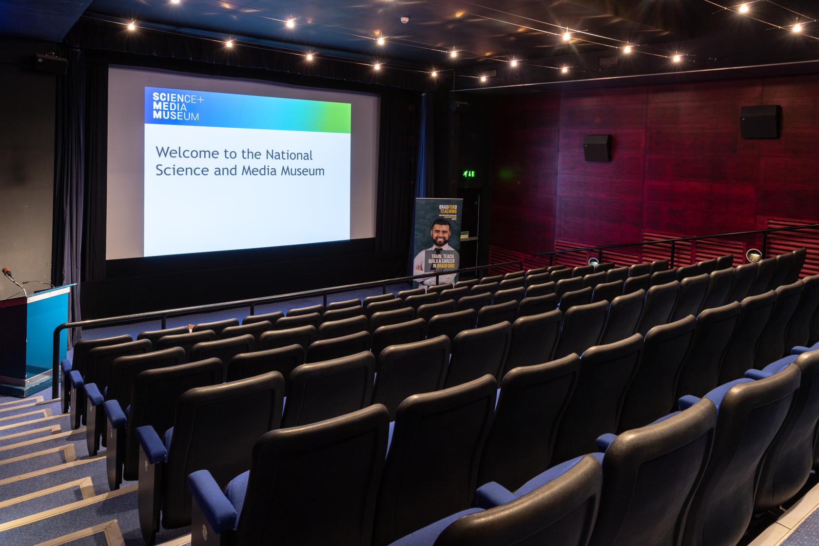 An auditorium with tiered seating, dark walls, and a large projection screen at The National Science and Media Museum.