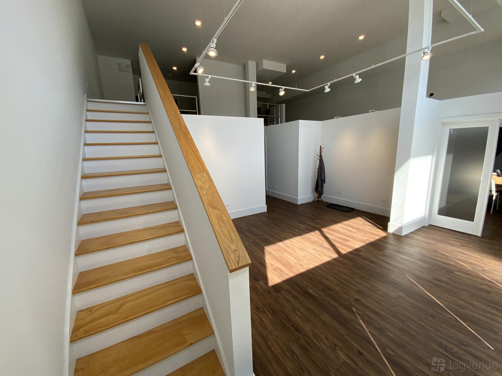 An art gallery with track lighting, white partition walls, and a wooden staircase at Watershed Studioworks.