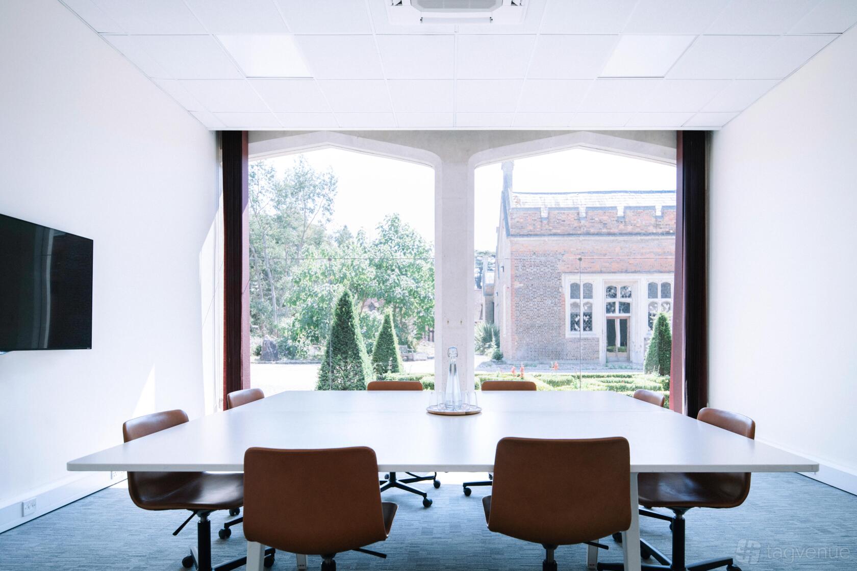 A castle meeting room with leather chairs, a large square table, and garden views at Ashridge House.