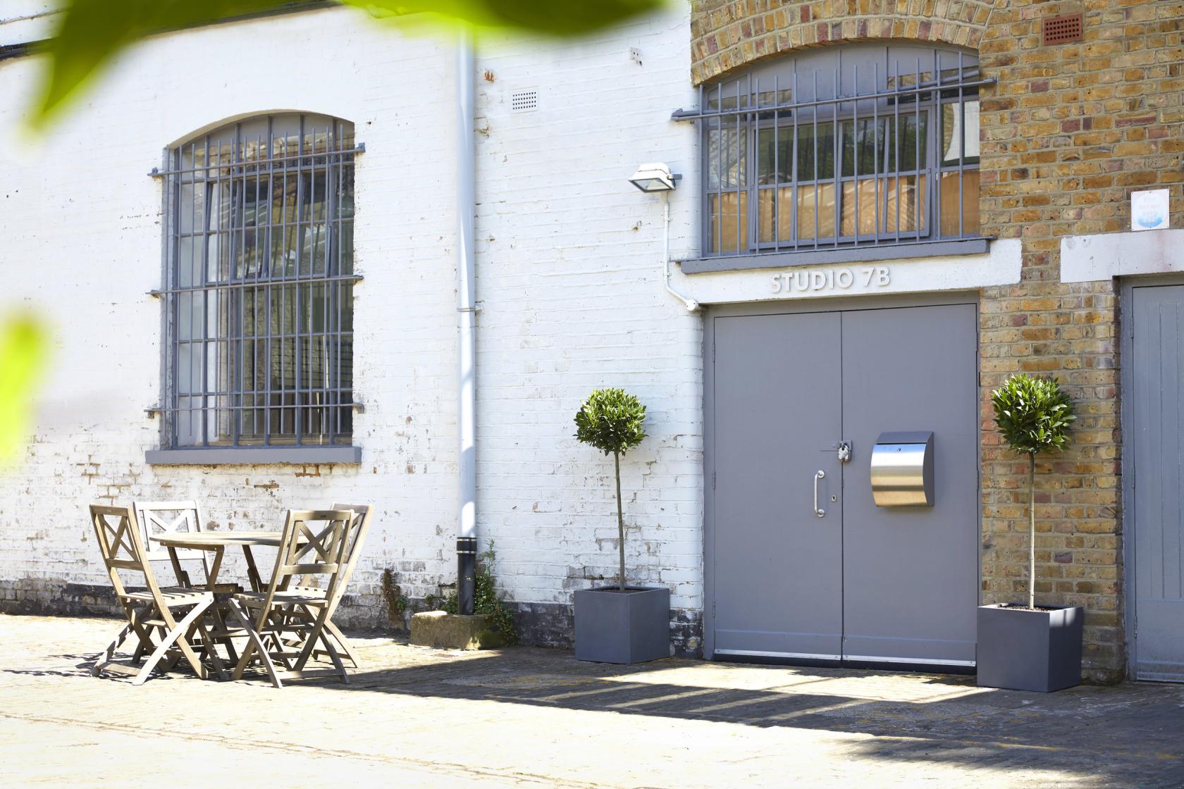 A film and photo studio with a grey double door, brick and white facade, and outdoor seating at Zap Studios.