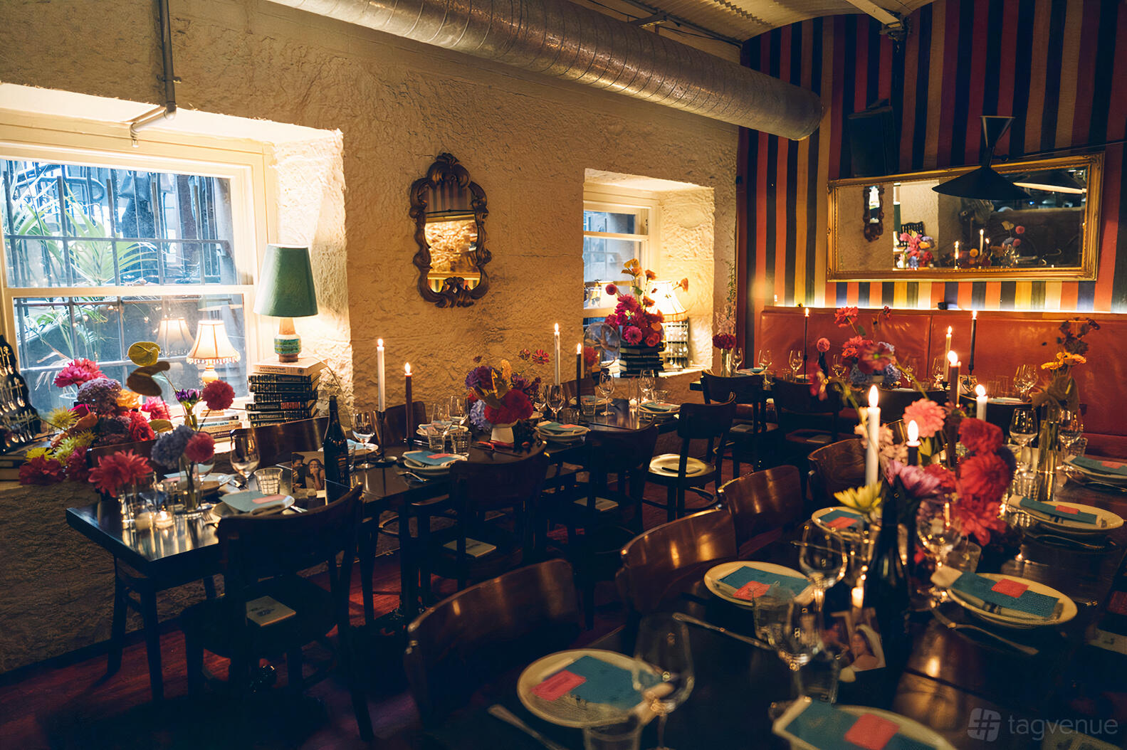 A restaurant with candlelit tables, floral centerpieces, striped accent wall, and large windows at The Moat.