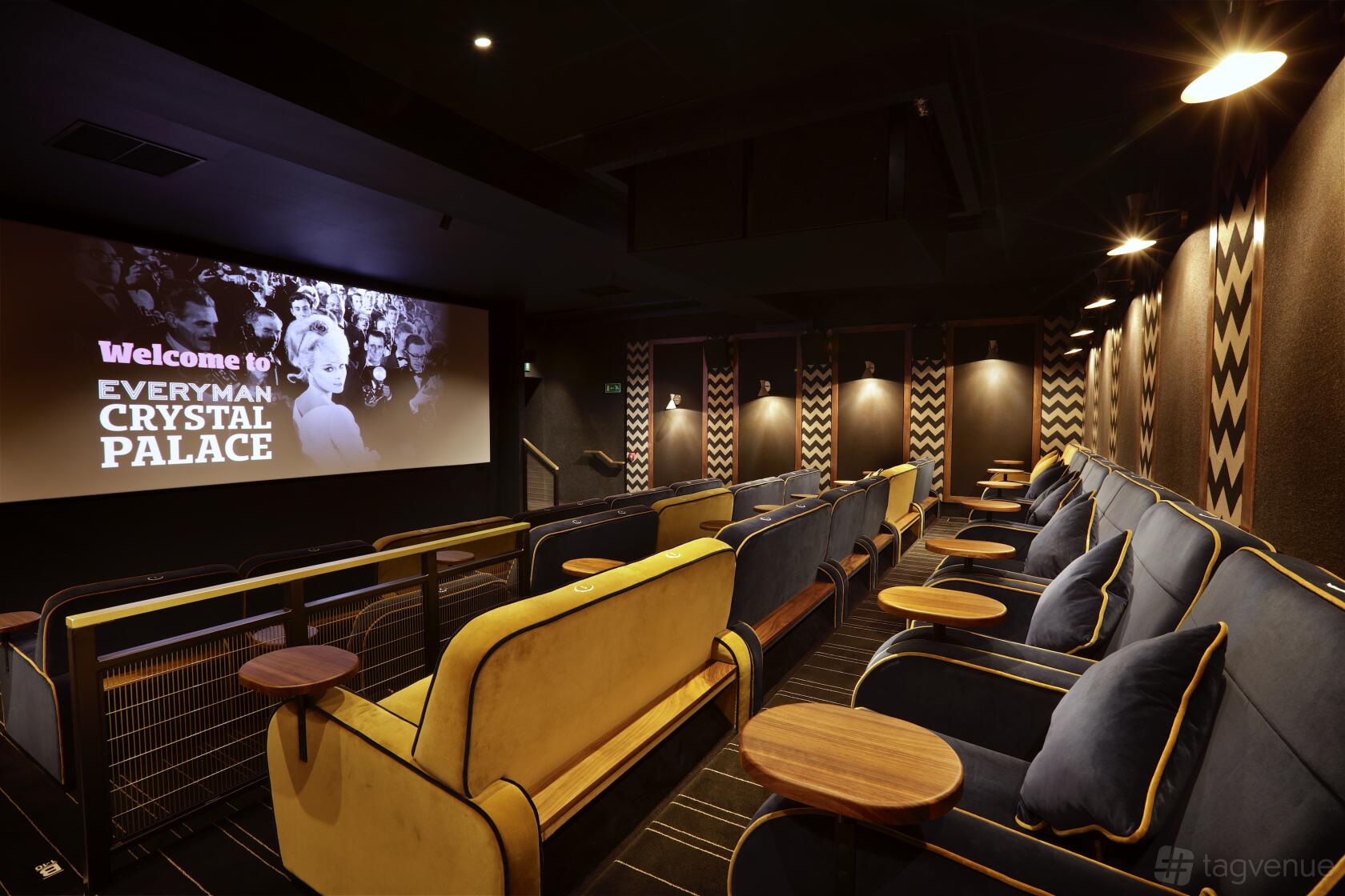 An auditorium with plush velvet sofas, small round wooden tables, and patterned acoustic wall panels at Everyman Crystal Palace.