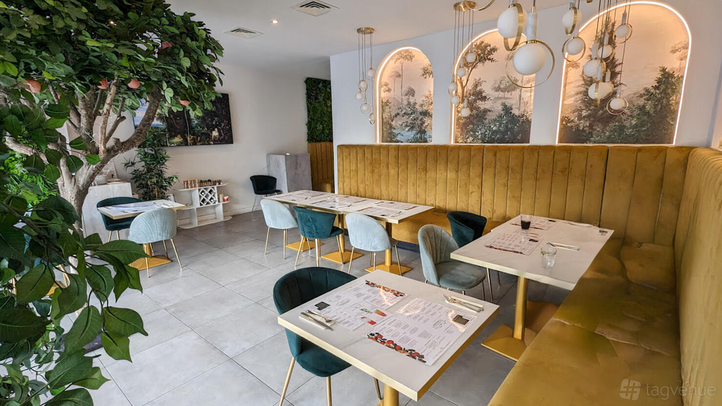 A restaurant dining area with gold velvet banquette seating, arched murals, and modern pendant lights at Bunchi.