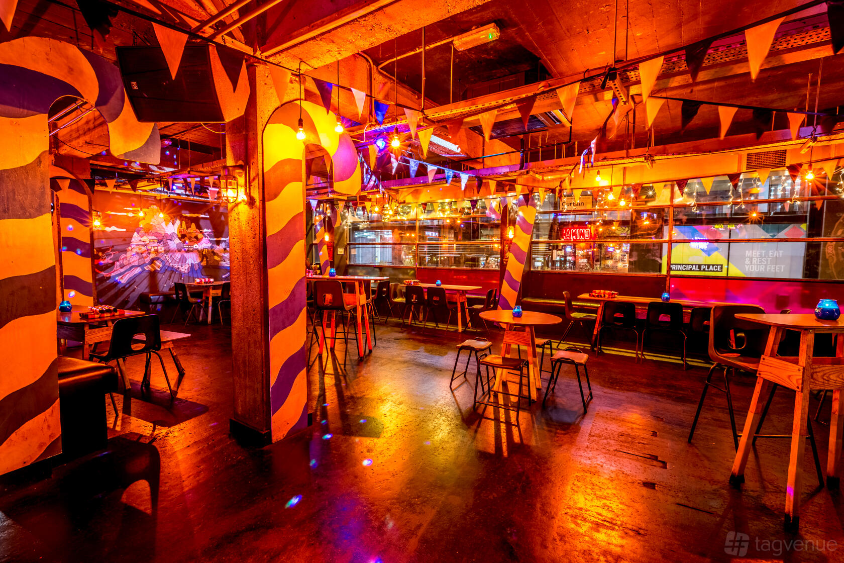 A nightclub cocktail bar with colorful striped columns, pendant lights, and high tables at Queen of Hoxton.