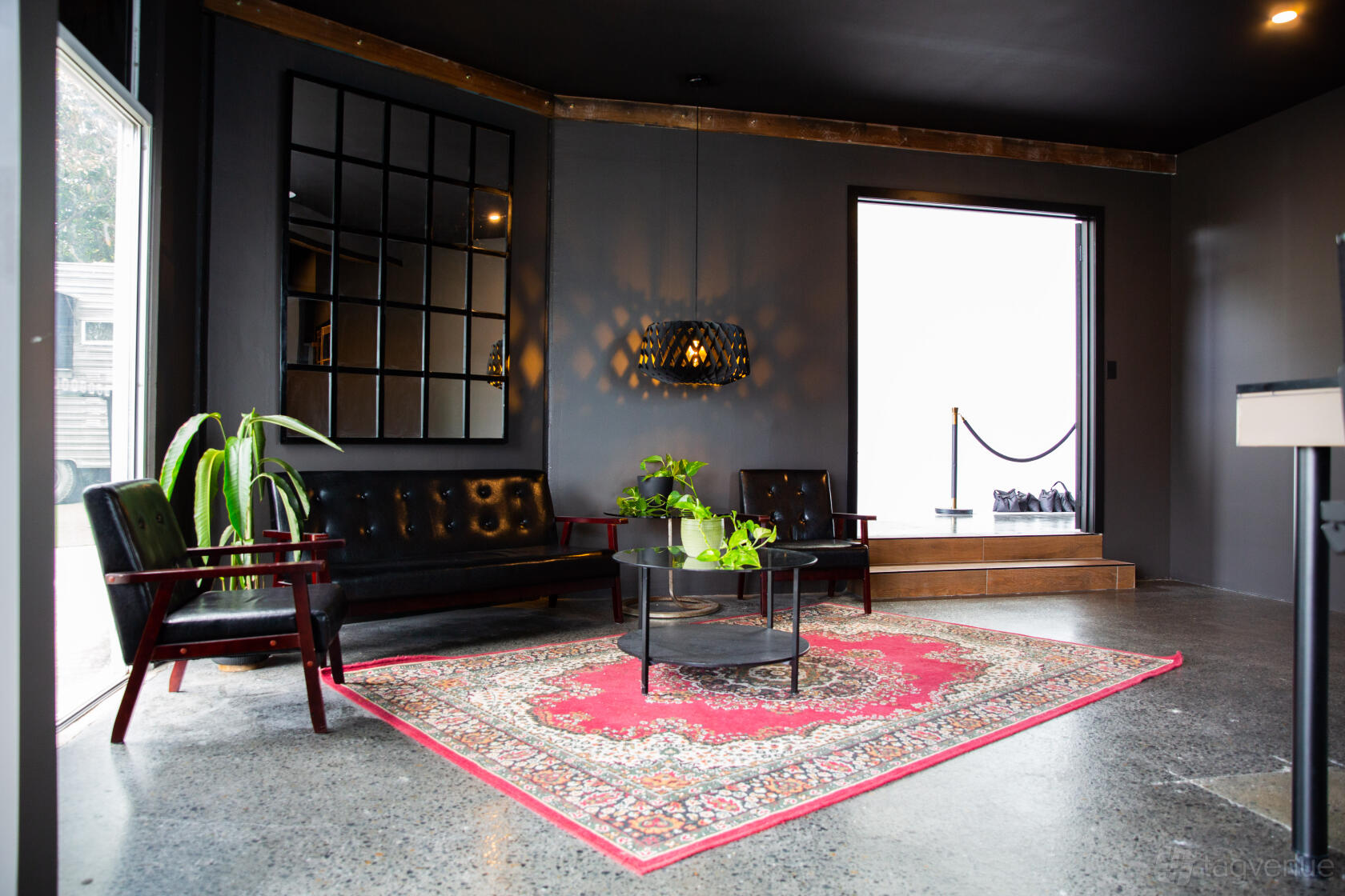 An event space with black lounge seating, a red patterned rug, large window, and potted plants at Focal House.