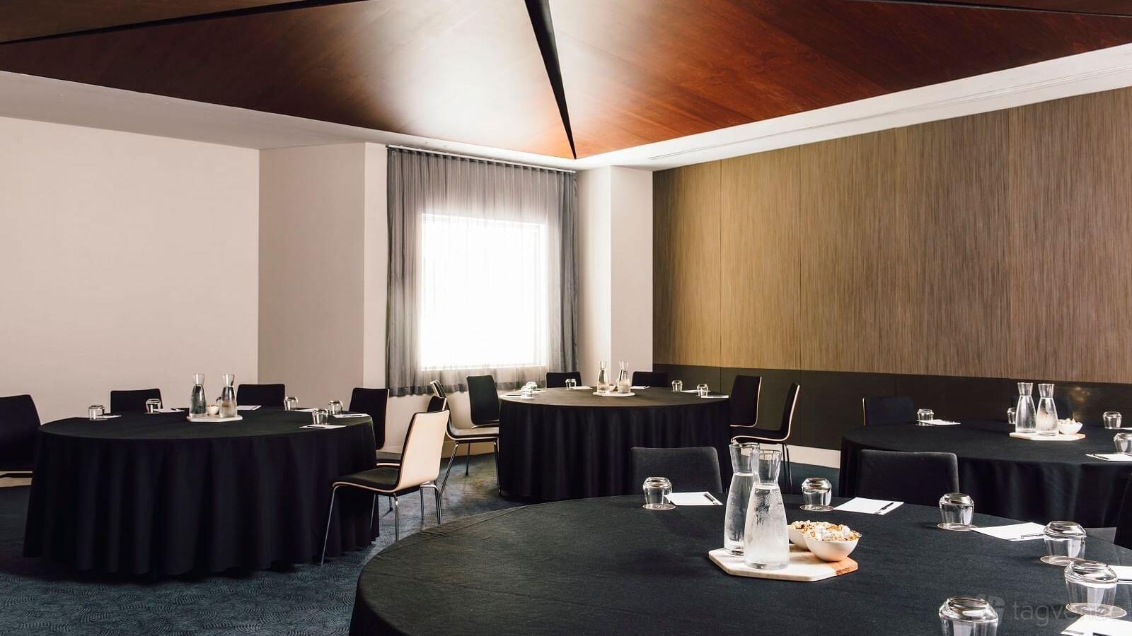 A meeting room with round tables covered in black linens, glass water jugs, and notepads at The Como Melbourne.