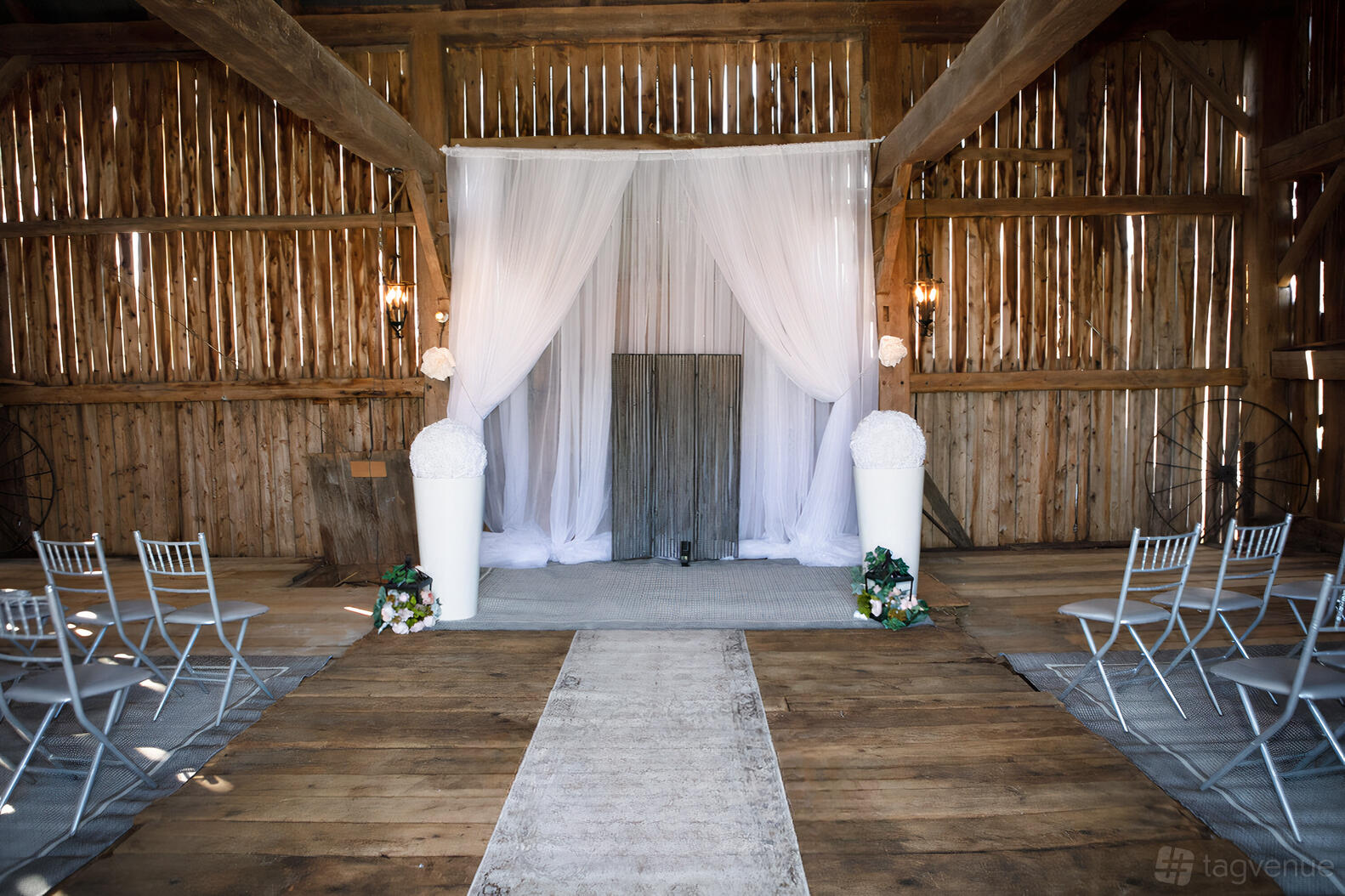 A rustic country house ceremony area with wooden walls, draped white fabric, and rows of silver chairs at Coach House Weddings.