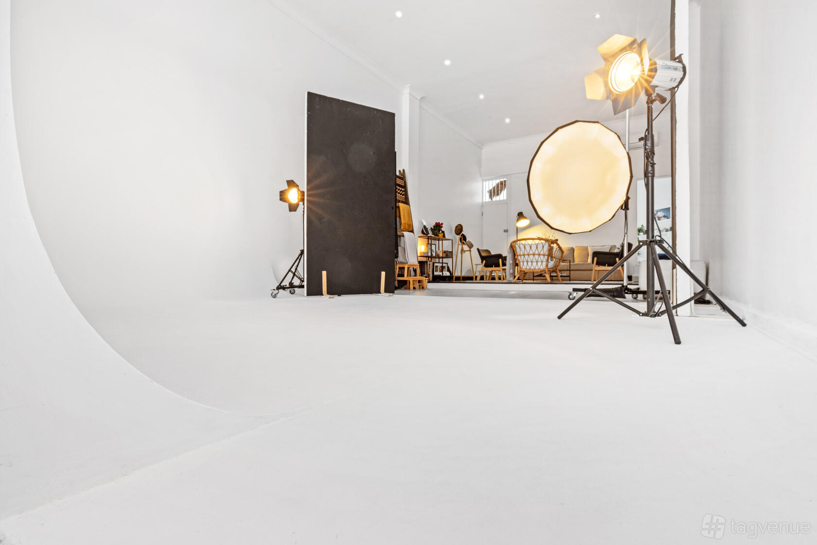 A photo studio with white cyclorama walls, studio lighting equipment, and a seating area at Portrait Hub.