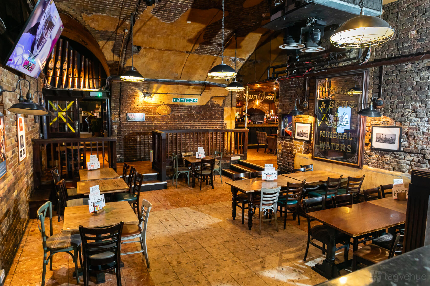 A pub with exposed brick walls, arched ceilings, wooden tables, and vintage signs at The Minories.