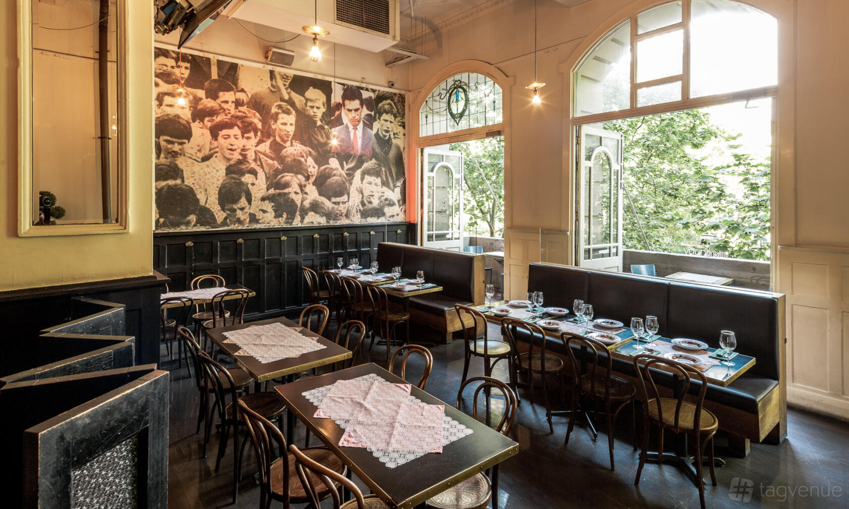 An event space in a restaurant with arched windows, wooden chairs, and long dining tables set for guests at Cookie.