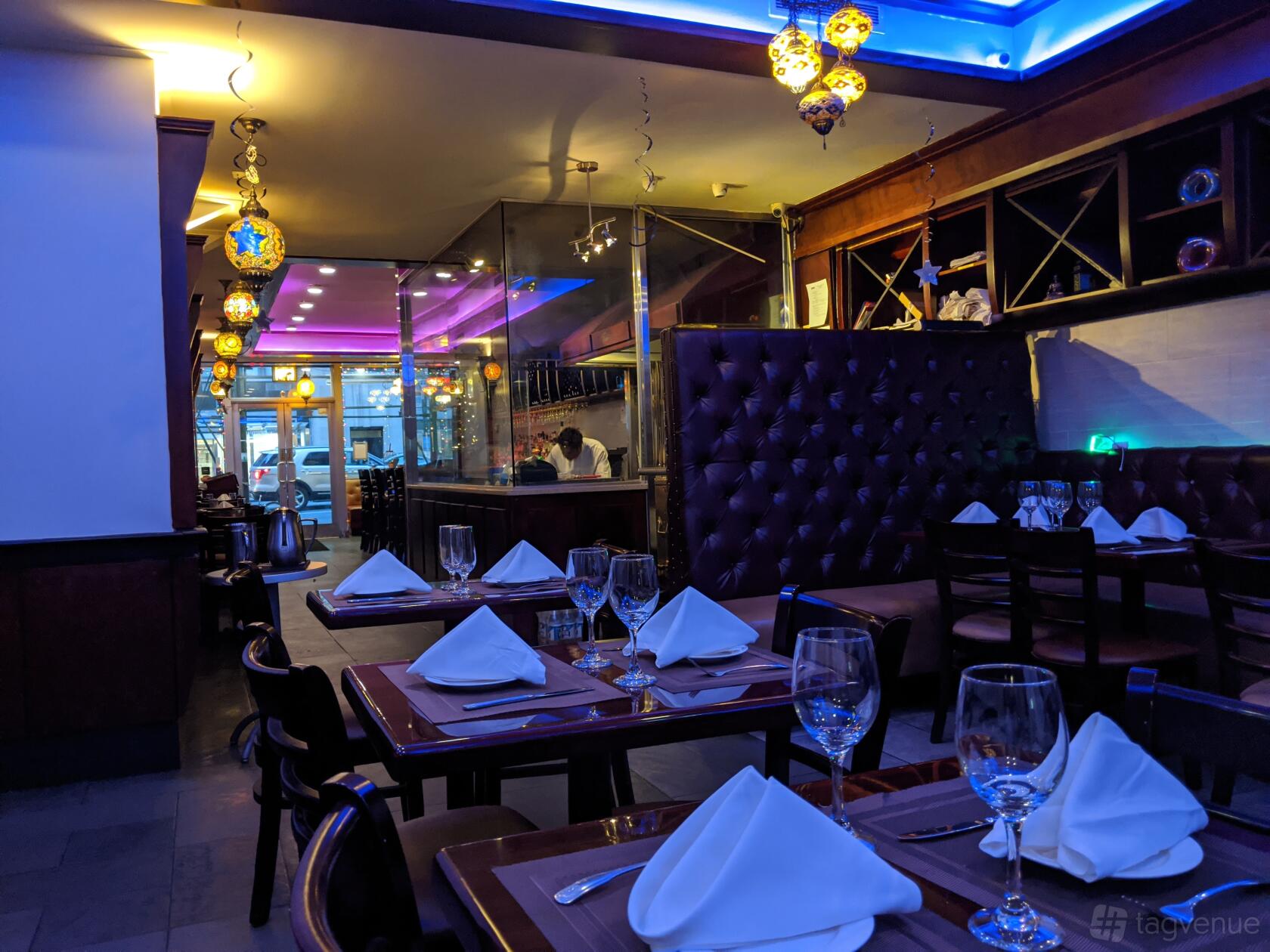 A restaurant dining area with white napkin place settings, glassware, tufted banquette seating, and hanging lanterns at Masala King.