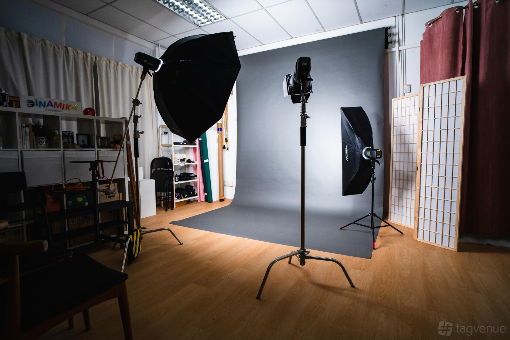 A photo studio with lighting equipment, a seamless grey backdrop, and wooden flooring at Dinamika Photo Studio.